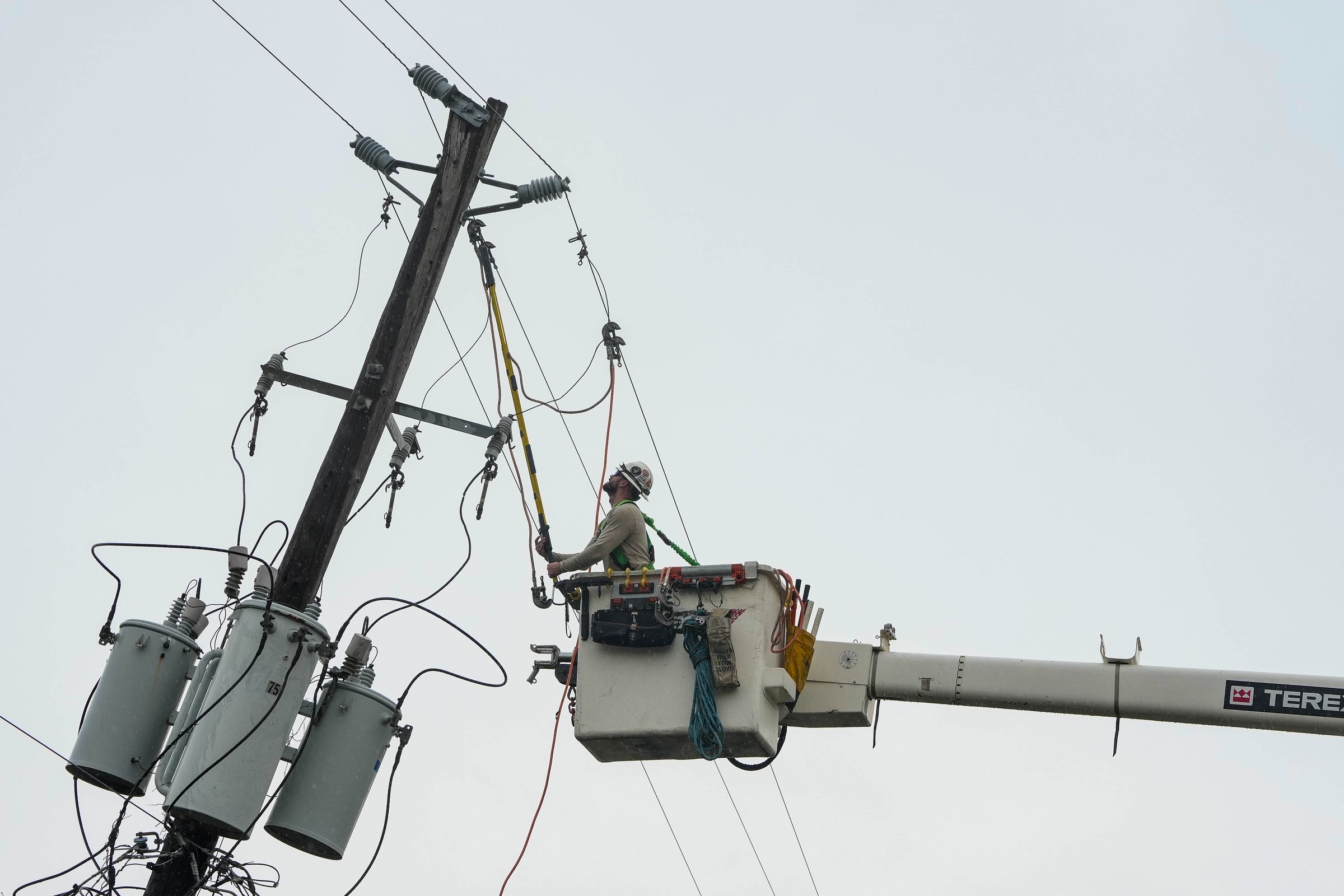 A crane lifts a worker up to a utility pole to repair power lines.