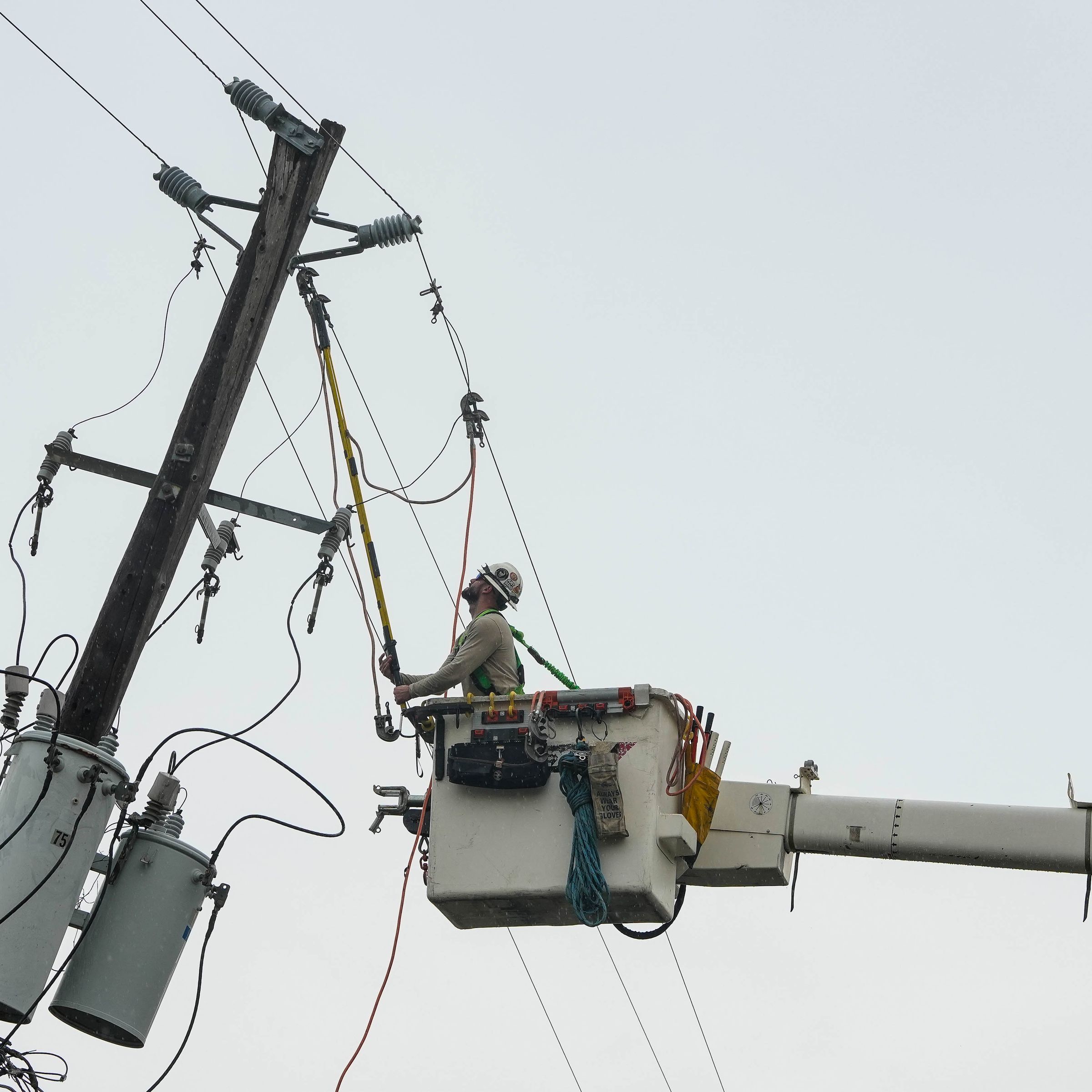 A crane lifts a worker up to a utility pole to repair power lines.