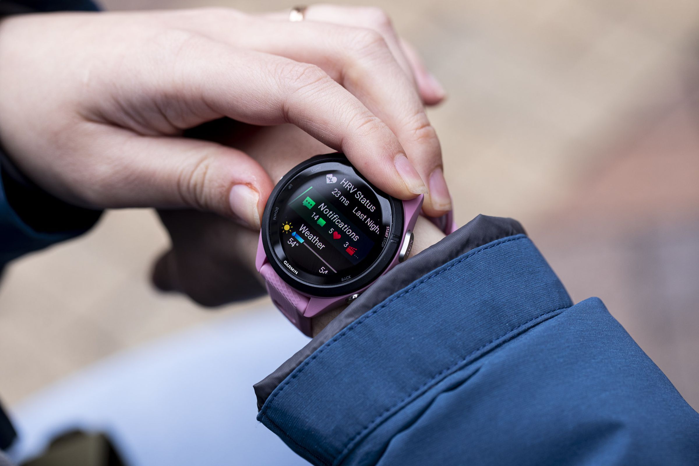 A close-up image of a pink Garmin Forerunner 265S on a woman’s wrist, just outside a blue raincoat.