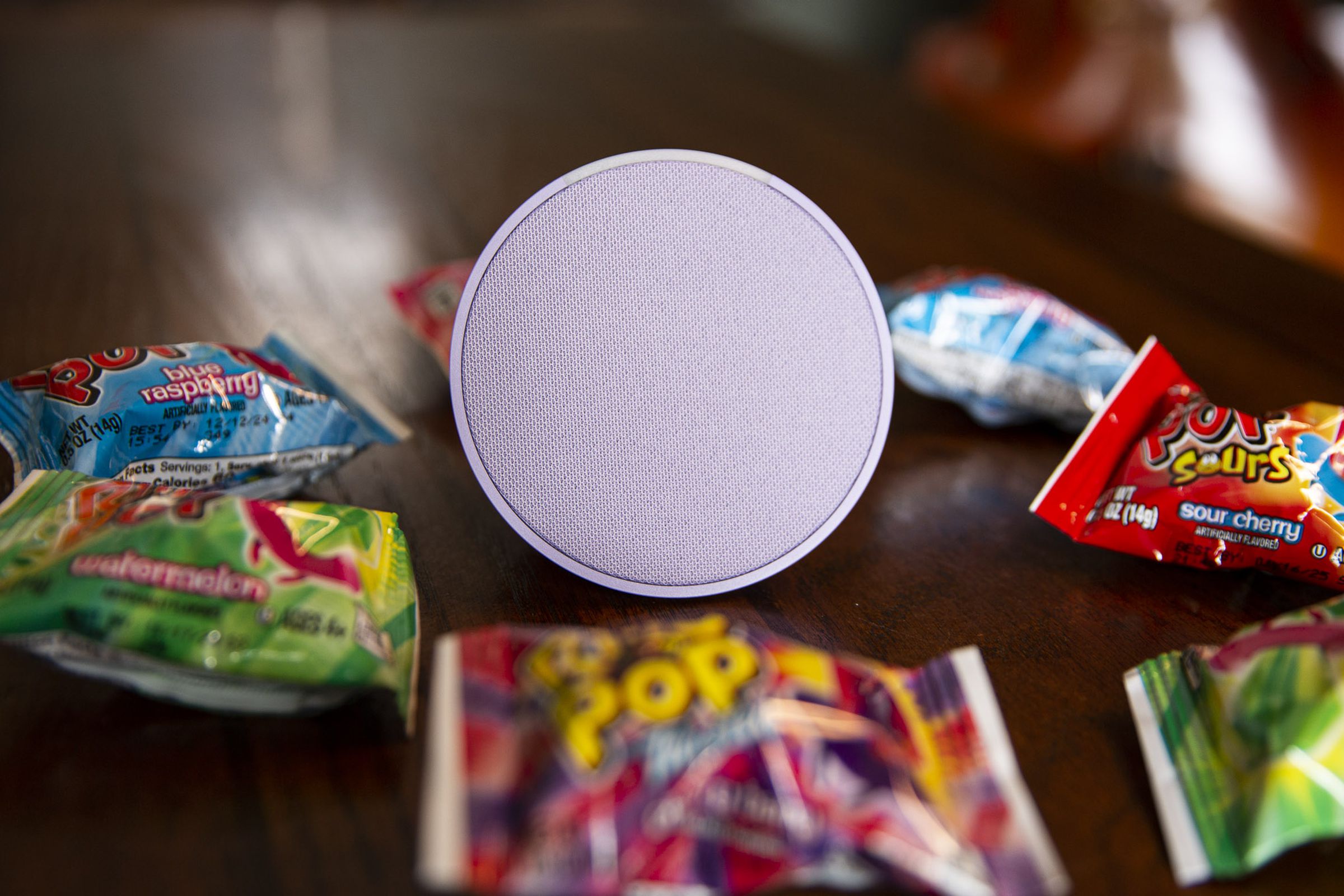 A purple Echo Pop smart speaker on a table surrounded by Ring Pop candy.