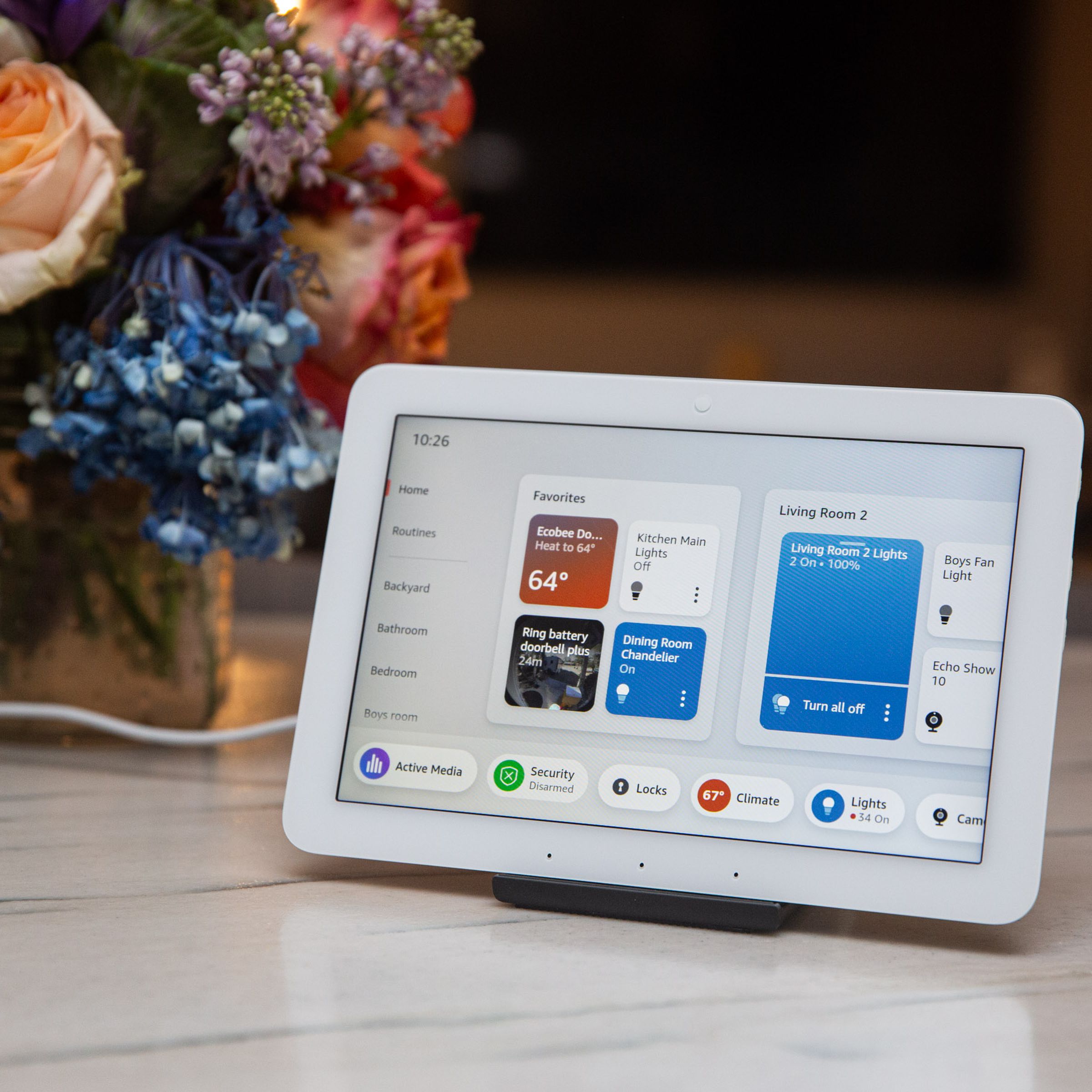 A small touchscreen tablet on a counter next to some flowers.