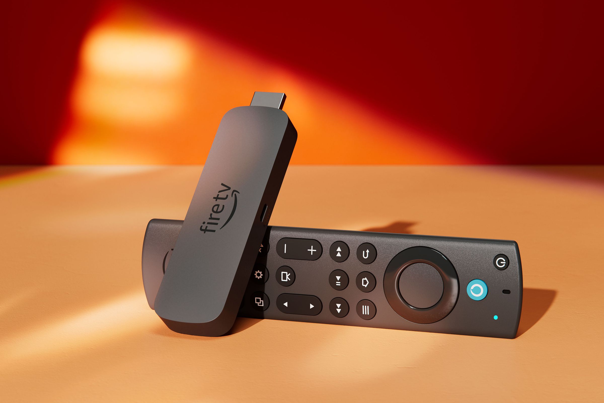 A close-up photo of the Amazon Fire TV Stick 4K Max resting on its side on a table against a red wall.