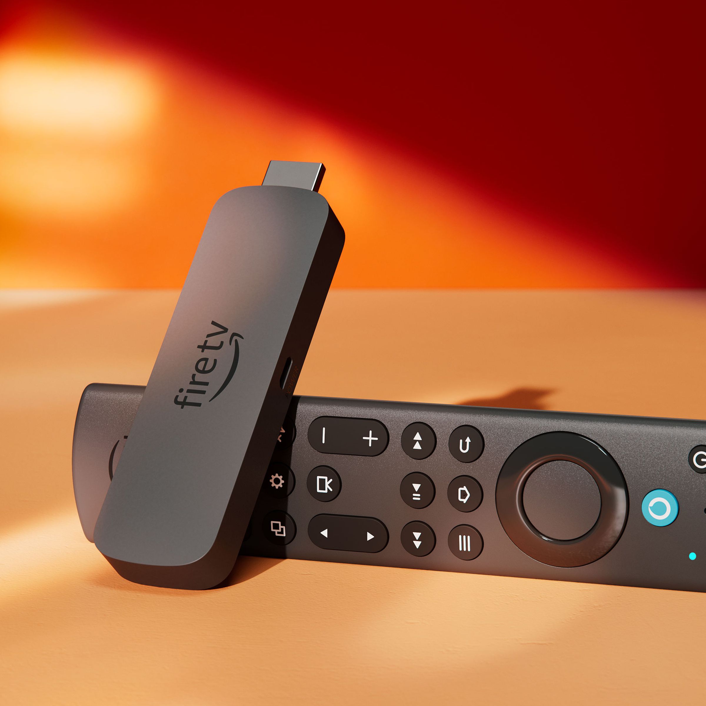 A close-up photo of the Amazon Fire TV Stick 4K Max resting on its side on a table against a red wall.