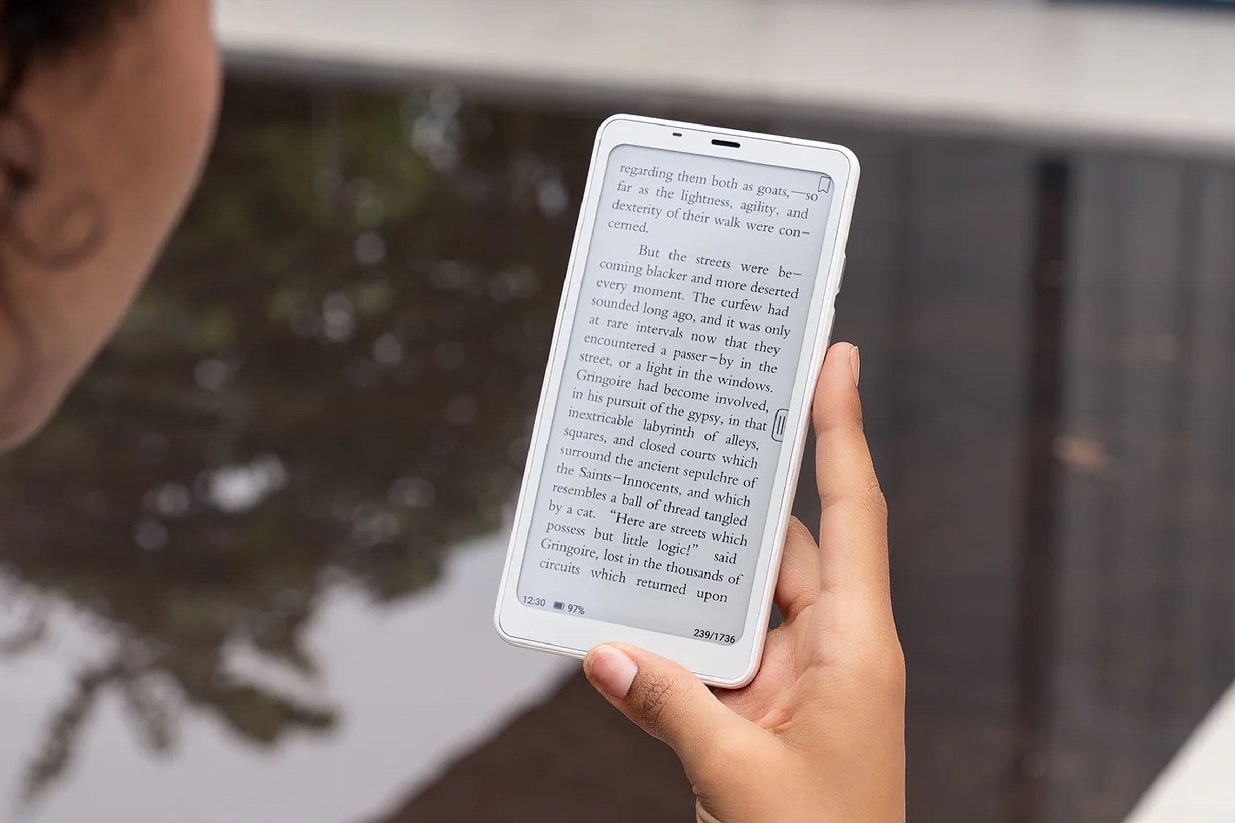 A photo of a person using a smartphone-like device near water.