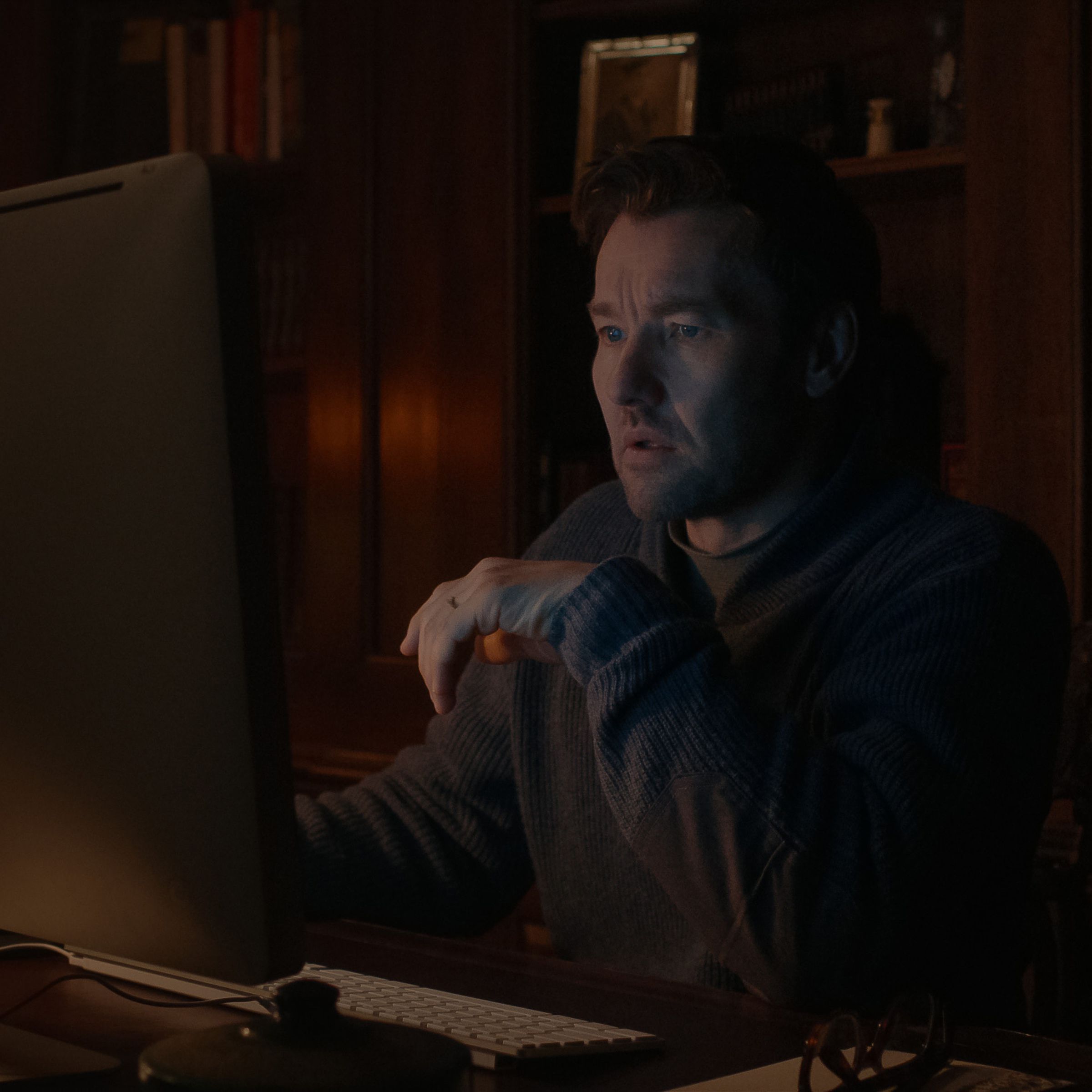 A man sitting in a dark room in front of his computer at a desk.