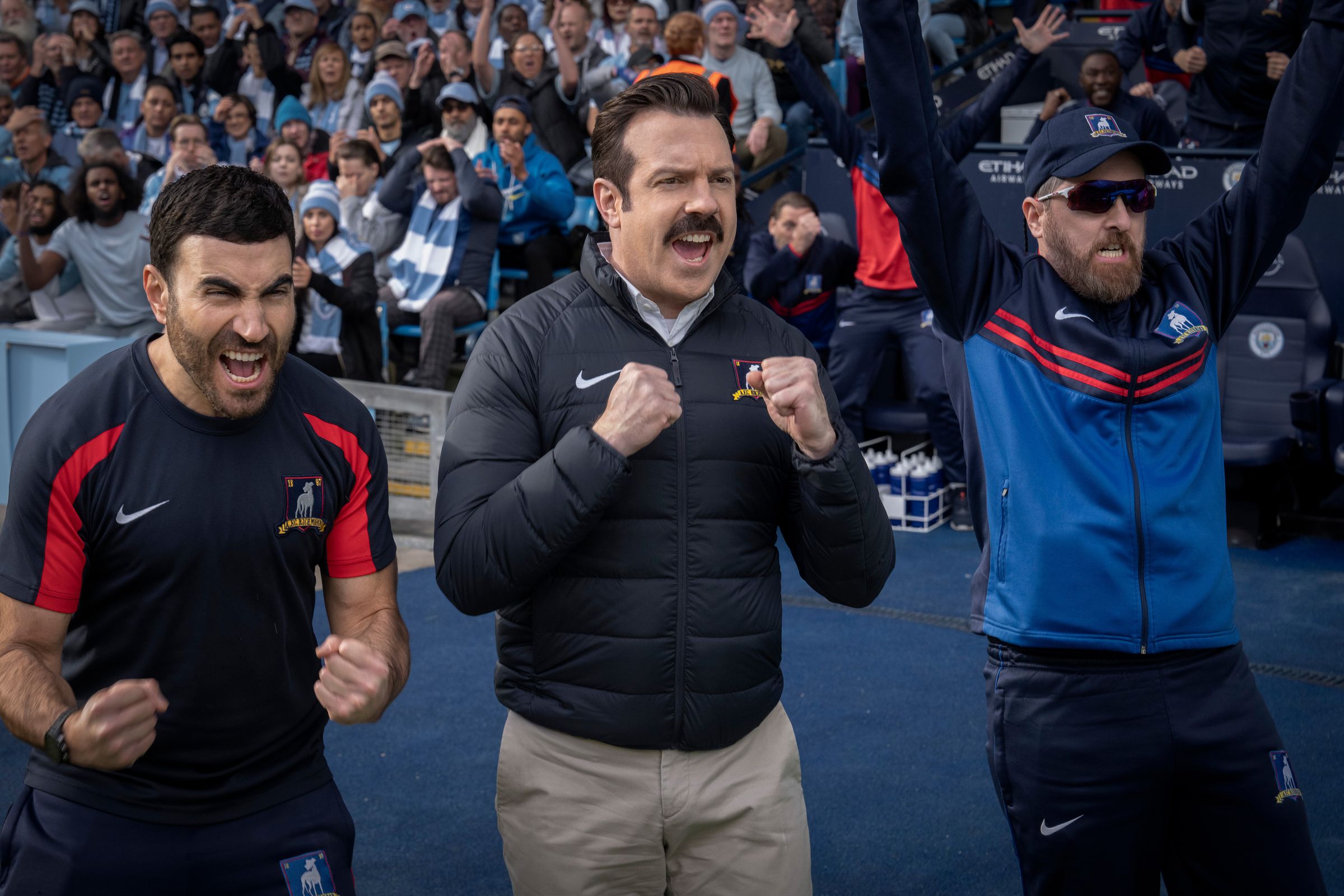 Three men standing on the sidelines of a football field cheering.