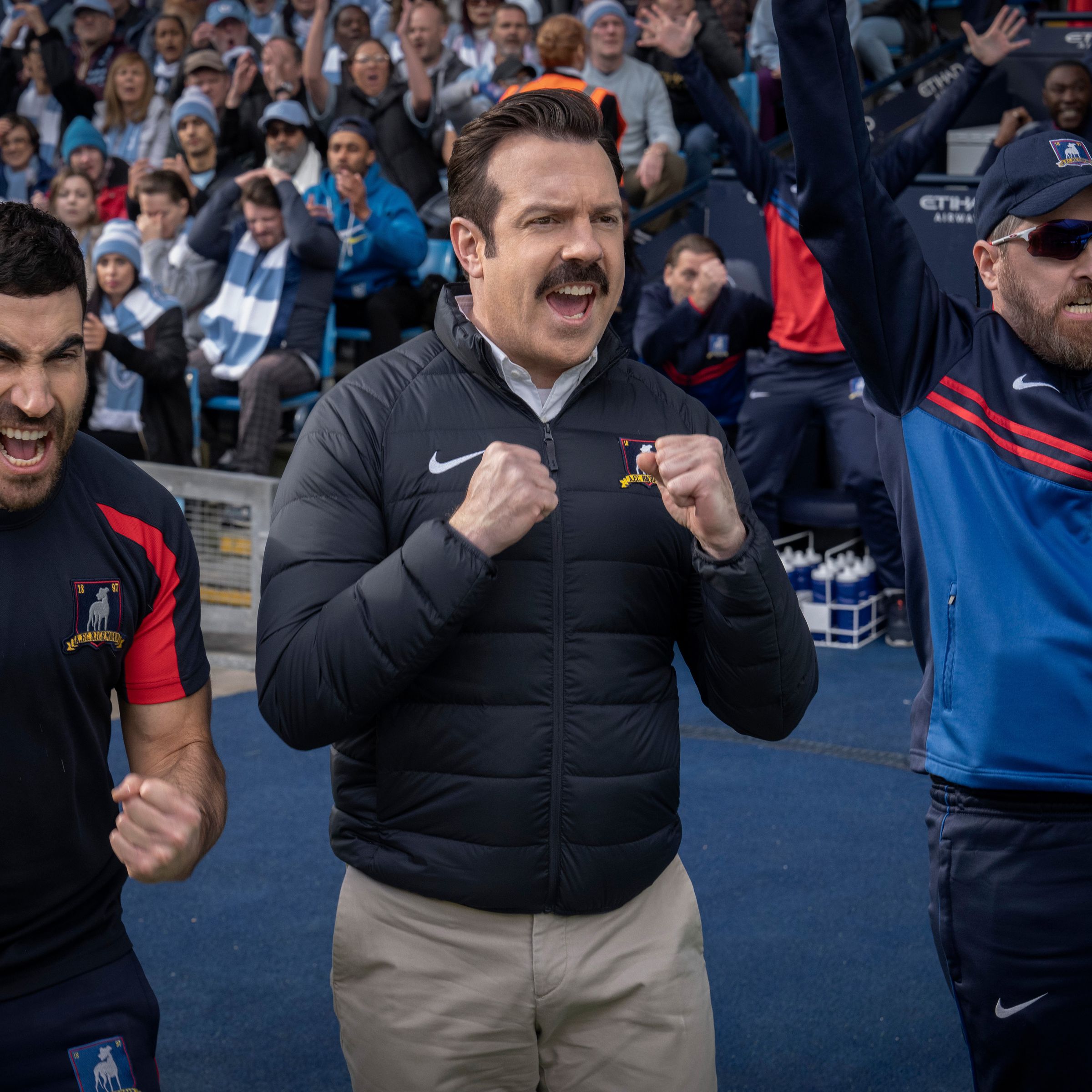 Three men standing on the sidelines of a football field cheering.